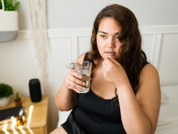 brown haired woman taking a pill holding a glass of water