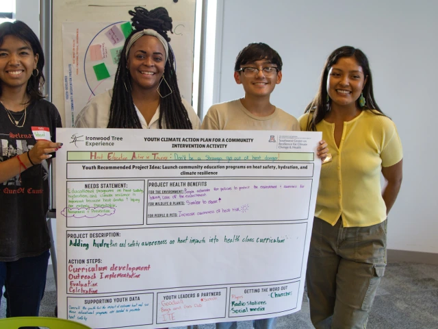 Four young people smiling while presenting a poster session of their work.