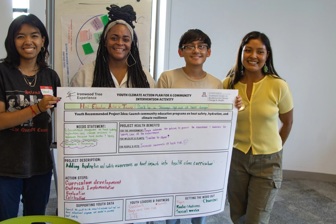 Four young people smiling while holding their poster developed during the workshop.